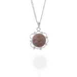 Ett silverhalsband, "Halsband med handslipad Hoburgsmarmor 32x23mm", har ett runt hänge med marmorerad rosa och grå sten i en blommig ram, visat med kedja och hänge reflekterade mot en vit bakgrund.