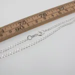 Pansarkedja 2,6mm Halskedja 50-70cm silverhalsband med karbinlås visas bredvid en trälinjal i tum, som visar dess längd.
