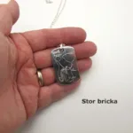 En hand håller i Hängsmycke Bricka AMS 800 i sterlingsilver, ett silverhalsband med ett rektangulärt medicintekniskt hänge graverat på svenska. Texten "Stor bricka" visas nedan på en vit bakgrund.