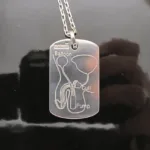 Hängsmycke Bricka AMS 800 i sterlingsilver är ett silverhalsband med ett graverat diagram över ett penisimplantat märkt Ballong, Manschett och Pump, mot en blank svart bakgrund.