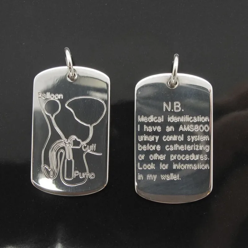 Hängsmycke Bricka AMS 800 i sterlingsilver innehåller två taggar: en med ett märkt AMS800-diagram över urinvägarna, den andra anger att bäraren har denna enhet och att han/hon ska titta i plånboken för mer information.