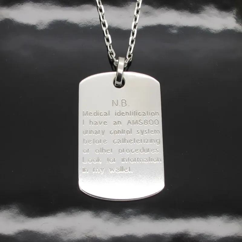 Hängsmycke Bricka AMS 800 i sterlingsilver är en medicinsk ID-bricka i silver på en kedja, graverad för att indikera att bäraren har en AMS 800 urinvägskontroll och för att kontrollera plånboken för mer information.