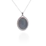 Halsband med handslipad Kalcedon 38x25mm är ett silverhalsband med ett ovalt, handskuret gråblått kalcedonhänge kantat av pärlor, mot en vit bakgrund med en subtil reflektion.