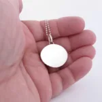 Närbild av en hand som håller i Halsband med handslipad Kalcedon 32x23mm på en pärlkedja, mot en vit bakgrund.