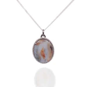 Ett halsband med silverkedja, "Halsband med handslipad Kalcedon 45x30mm", har en oval, handpolerad ädelsten av kalcedon i brunt, blått och gräddvitt infattad i en dekorativ silverinfattning mot en vit bakgrund.