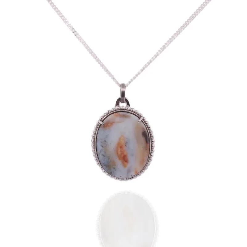 Ett halsband med silverkedja, "Halsband med handslipad Kalcedon 45x30mm", har en oval, handpolerad ädelsten av kalcedon i brunt, blått och gräddvitt infattad i en dekorativ silverinfattning mot en vit bakgrund.