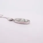 Porslinssmycke - Gröna Anna" är ett ovalt silverhänge med ett bladgrönt mönster, hängande i en tunn silverkedja mot en vit bakgrund.