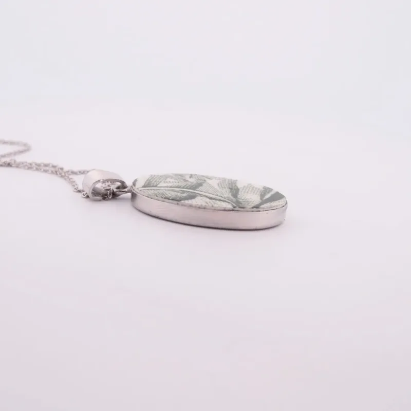 Porslinssmycke - Gröna Anna" är ett ovalt silverhänge med ett bladgrönt mönster, hängande i en tunn silverkedja mot en vit bakgrund.