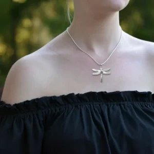 191475049-origpic-e35f43 - Fredrix Design & Smyckerian En person iklädd en svart off-the-shoulder topp och Hängsmycke Trollslända - Kulkedja 45cm silver trollslända hänge halsband står utomhus med grönska suddigt i bakgrunden.