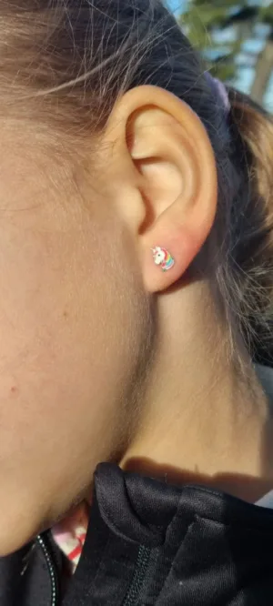 Närbild av ett barns öra med Örhänge med stift - Enhörning, ett litet färgglatt örhänge i form av en enhörning. Solljuset framhäver örat och örhänget med en del av barnets kind och hals synliga.