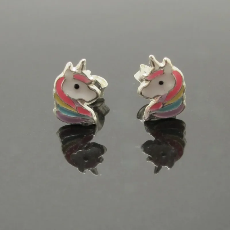 Ett par "Örhänge med stift - Enhörning" enhörningsformade stiftörhängen med vita ansikten, rosa manar och regnbågsdetaljer visas på en reflekterande svart yta.