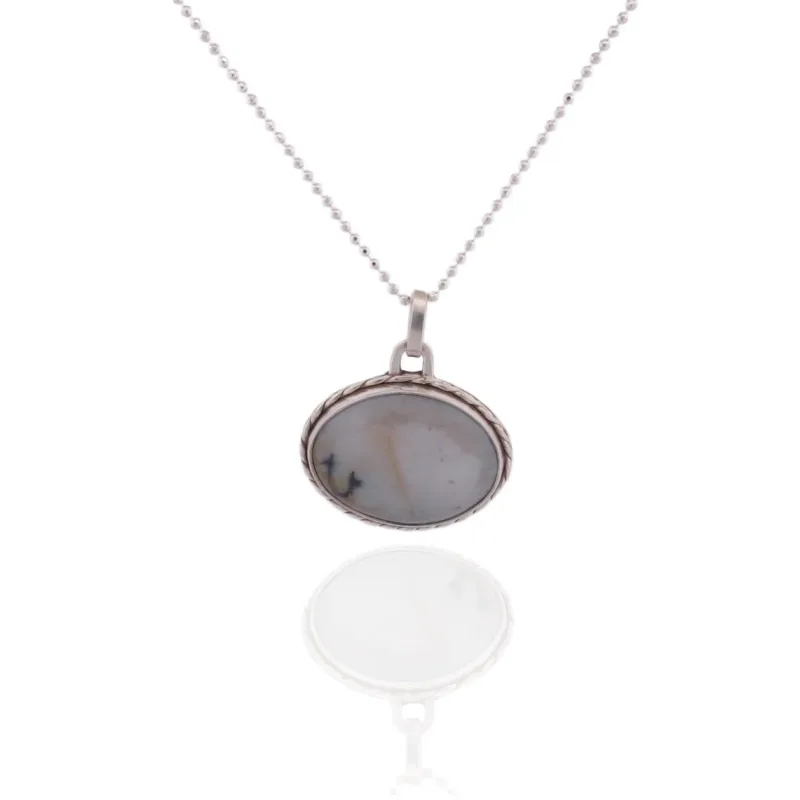Ett silverhalsband med namnet "Halsband med handslipad Kalcedon" har ett runt hänge med en handpolerad kalcedonsten med mjuka grå och beige ådringar, som visas på en reflekterande vit yta.