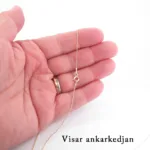 En hand håller i Hängsmycke i 14K Guld Gotland på en skir guldkedja mot en vit bakgrund. Personen bär en guldring och längst ned till höger står det "Visar ankarkedjan".