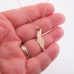 En hand visar Hängsmycke i 14K Guld Gotland, ett guldhalsband med ett hänge format som Gotland. Personen bär en guld- och silverring på ringfingret.