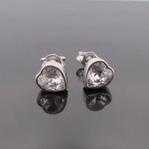 Örhänge med stift Kristallhjärta: Silverfärgade hjärtformade örhängen med klara kristaller, visade på en reflekterande svart yta.