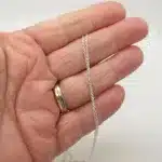 En hand med en ring i guld och silver håller i Ankarkedja 1,2 mm Halskedja 38-50 cm, ett fint halsband med silverkedja, mot en vit bakgrund.