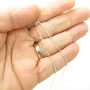 En hand med en guldring på ringfingret håller i Ankarkedja 1,2mm Halskedja 38-50cm silverhalsband mot en vit bakgrund.