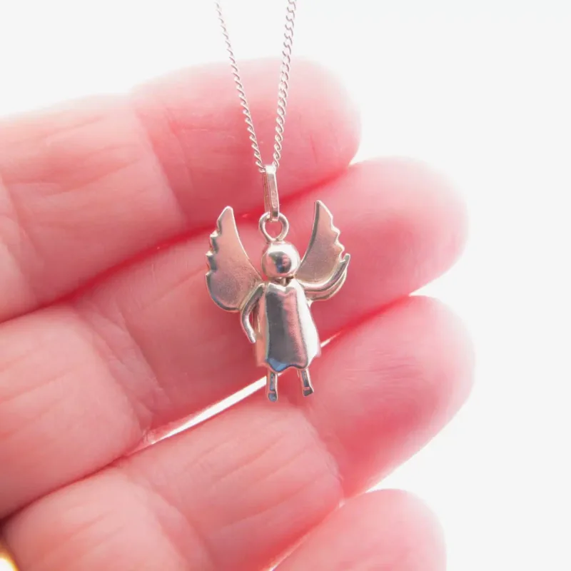 En hand håller i Handgjord Silverängel 25mm, ett änglahänge i silver med utsträckta vingar och runt huvud, fäst vid ett delikat kedjehalsband mot en enkel, ljus bakgrund.
