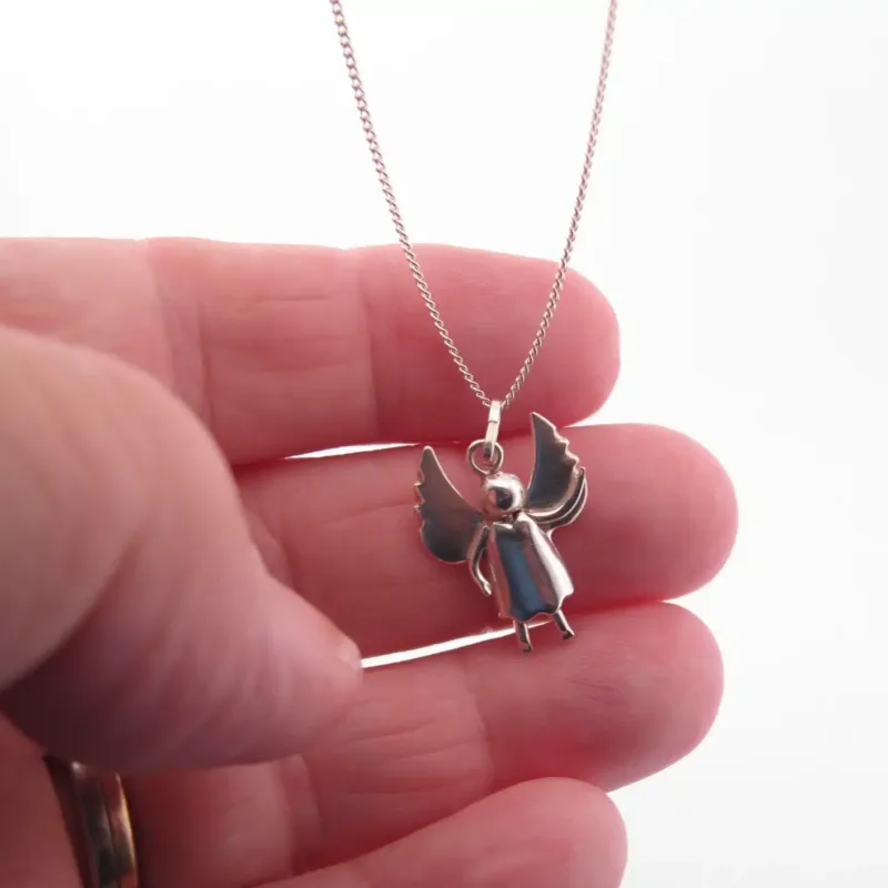 En hand håller i Handgjord Silverängel 25mm, ett silverhalsband med ett litet änglahänge med utsträckta vingar, mot en vit bakgrund.