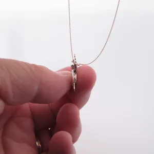 Närbild av en hand som håller i Handgjord Silverängel 25mm, ett delikat halsband med en tunn kedja och ett platt, änglalikt silverhänge mot en vit bakgrund.
