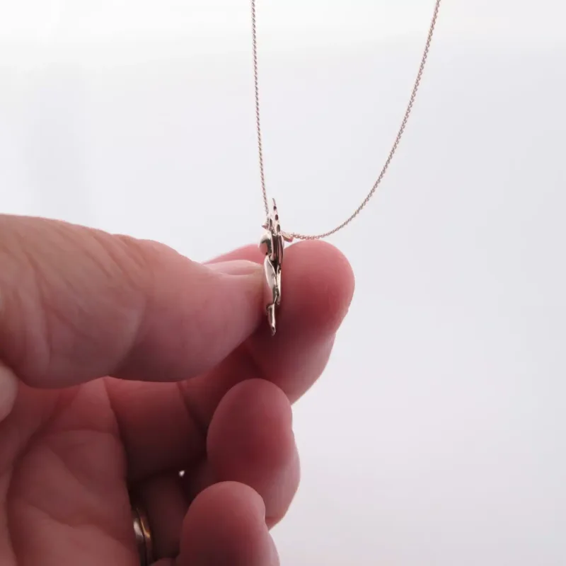 Närbild av en hand som håller i Handgjord Silverängel 25mm, ett delikat halsband med en tunn kedja och ett platt, änglalikt silverhänge mot en vit bakgrund.