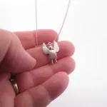 En hand visar Handgjord Silverängel 25mm, ett delikat silverhalsband med ett ängelhänge med utsträckta vingar, mot en vit bakgrund.
