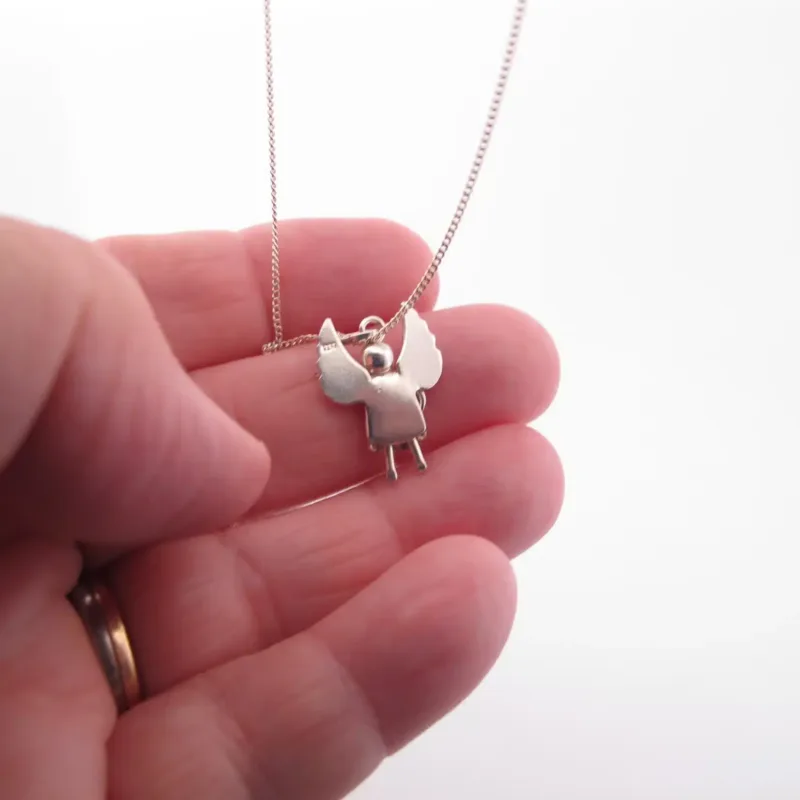 En hand visar Handgjord Silverängel 25mm, ett delikat silverhalsband med ett ängelhänge med utsträckta vingar, mot en vit bakgrund.