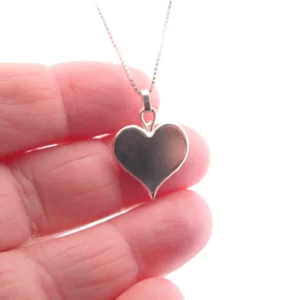 Närbild av en hand som håller i hänget Handgjort Silverhjärta 27x15mm på en fin kedja mot en vit bakgrund.