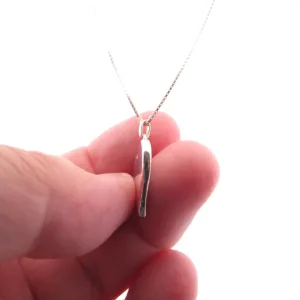 En hand håller i Handgjort Silverhjärta 27x15mm, ett delikat silverhalsband med ett tunt, vertikalt hjärtformat hänge, mot en vit bakgrund.