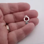 En hand håller i Silverberlock Kvinnosymbol-hänget, med två ringar på fingret, mot en vit bakgrund.