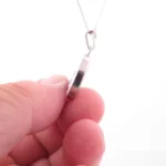 En hand håller i kanten av Porslinsmycke - Dresden 25x19mm silversmycke på en kedja, mot en vit bakgrund.