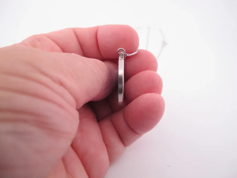 En hand håller Porslinssmycke - Gustavsberg 24mm, ett elegant runt silverörhänge, mot en vit bakgrund.