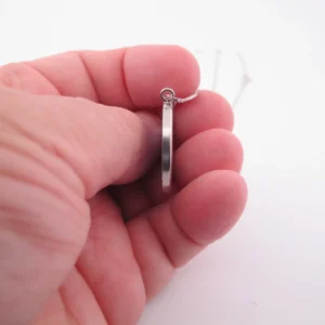 En hand håller Porslinssmycke - Gustavsberg 24mm, ett elegant runt silverörhänge, mot en vit bakgrund.