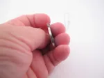 En hand håller i Porslinssmycke - Gustavsberg 24mm, ett tunt silverörhänge, mot en vit bakgrund.
