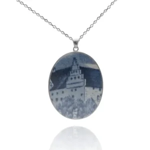 Porslinssmycke - Gustavsberg: Ovalt hängande halsband med en blåvit bild av ett slott med tak och träd, fäst på en tunn silverkedja.