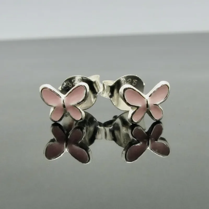 Ett par silverörhängen i form av fjärilar med vingar i rosa emalj, presenterade på en reflekterande yta.