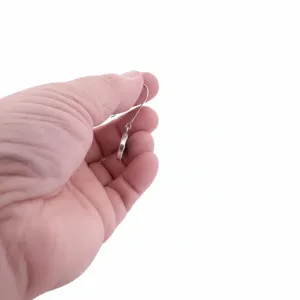En hand håller Örhänge med porslin - Adam örhänge, en enkel silverring, mot en enfärgad vit bakgrund.
