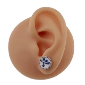 Örhänge med stift Krona - Dresden visas på ett realistiskt, köttfärgat modellöra, med en rund design med ett blått blommotiv inramat av en dekorativ silverkant.