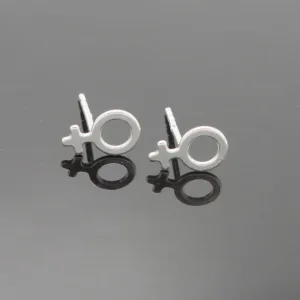 Ett par Örhänge med stift - Kvinnosymbol, silverörhängen formade som den kvinnliga könssymbolen, är placerade på en reflekterande mörk yta och visar sina speglingar.
