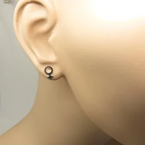 Närbild på en skyltdockas öra med Örhänge med stift - Kvinnosymbol, ett litet svart örhänge format som den kvinnliga könssymbolen. Bakgrunden är enfärgad och ljus.