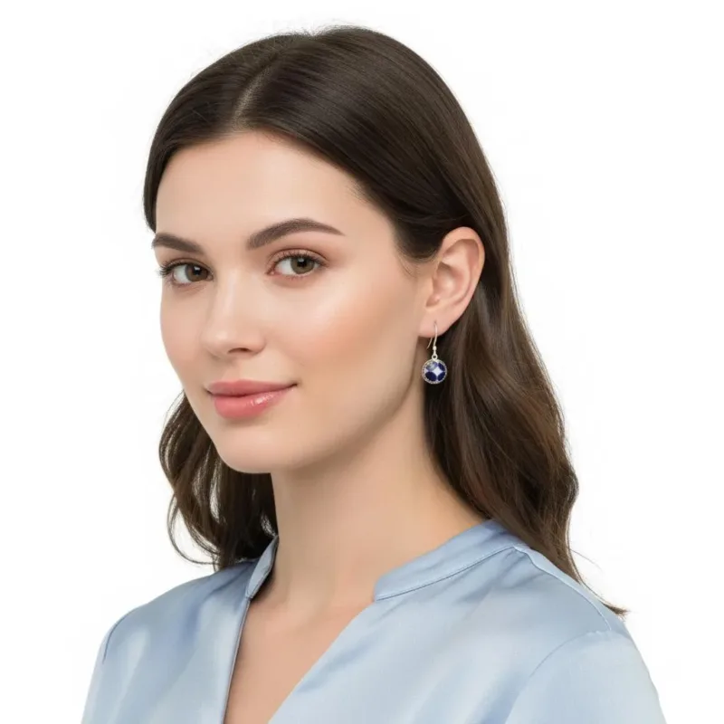 En kvinna med långt brunt hår, klädd i ljusblå blus och Örhänge Krona med porslin - Adam örhängen, ler lätt och tittar in i kameran mot en vit bakgrund.