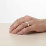 En hand som bär Fingerring hamrad yta i äkta silver vilar på en ljus träyta, det enkla silverbandet visas upp mot en vit bakgrund.