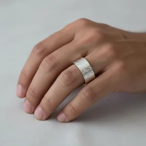 En hand med prydligt klippta naglar vilar på en ljus yta och visar upp Fingerring hamrad yta i äkta silver - en bred, hamrad silverring med en strukturerad, matt yta på långfingret.