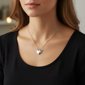 En kvinna med svart topp och Handgjort Silverhjärta med vingar - ett silverhjärtformat hänge med vingar - poserar inomhus i dämpad belysning.