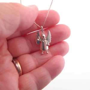 En hand håller i Handgjord Silverängel 26mm - en änglalik berlock i silver med vingar och runt huvud - på en kedja. Bakgrunden är vit och personen bär en guldring.