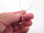 En hand håller i Handgjord Silverängel 26mm, ett handgjort silverhalsband med änglaliknande hänge, mot en vit bakgrund.