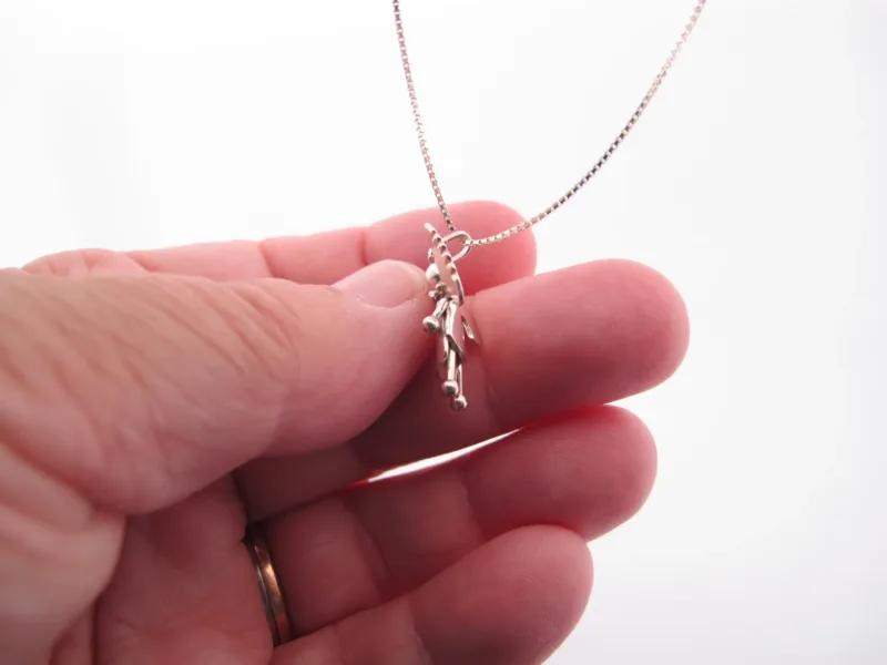 En hand håller i Handgjord Silverängel 26mm, ett handgjort silverhalsband med änglaliknande hänge, mot en vit bakgrund.