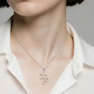 En kvinna med kort mörkt hår bär en vit skjorta med krage och ett silverhalsband med ett hänge i form av en kemisk struktur.