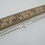 Kulkedja 2mm Halskedja 50-60cm silverkulhalsband med karbinlås visas bredvid en trälinjal märkt i centimeter och millimeter, vilket illustrerar dess ungefärliga längd på 50-60cm.