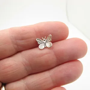 En närbild av en hand som håller Örhänge med stift - Fjäril, ett litet fjärilsformat örhänge i silver, mot en vit bakgrund.